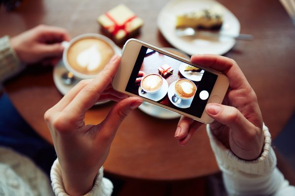 Two coffees, cheesecake and small giftbox on cellphone display held by one of dates